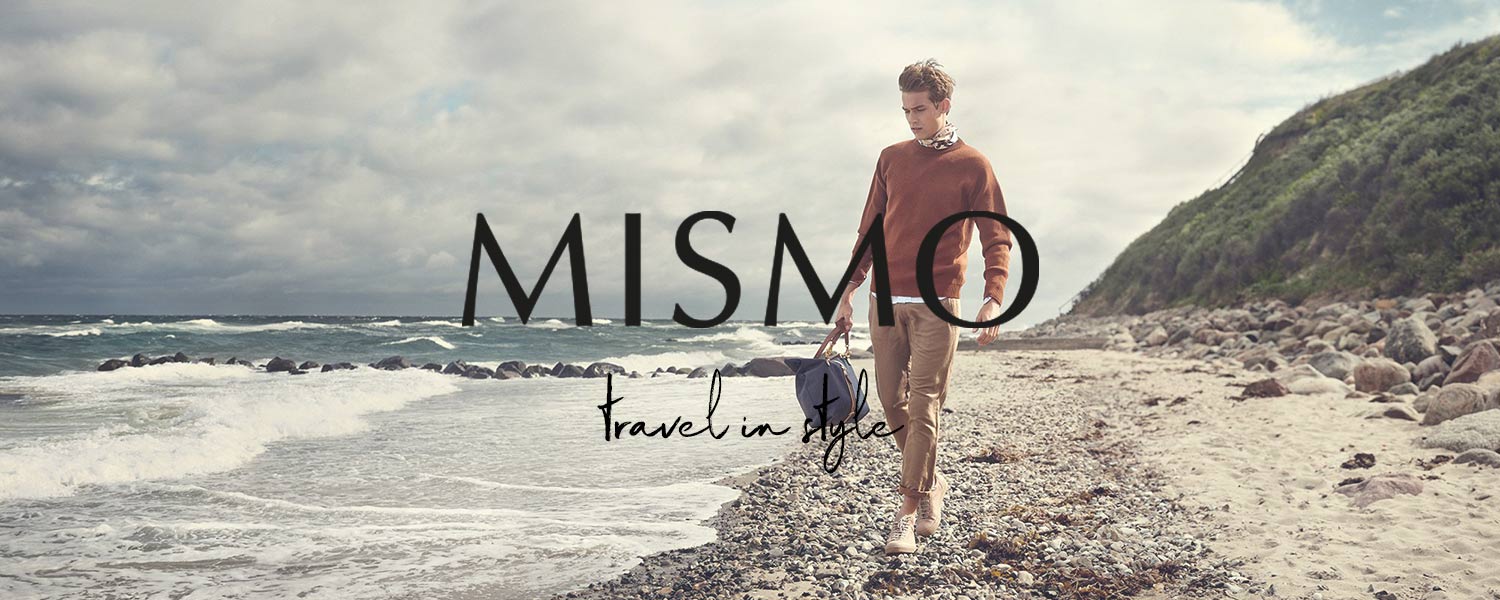 Ein junger Mann steht am Strand und hält eine Mismo Tasche in der Hand
