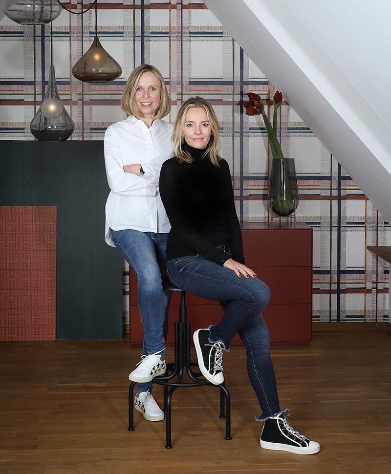 Martina Göbl und Stefanie Raum, die zwei Gründerinnen von RAUM concept store sitzen auf Hockern in den Räumlichkeiten des RAUM concept stores