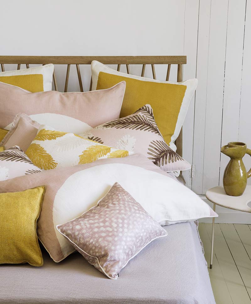 Élitiskissen in frischen Gelb- und Rosatönen sind dekorativ auf einem Bett arrangiert