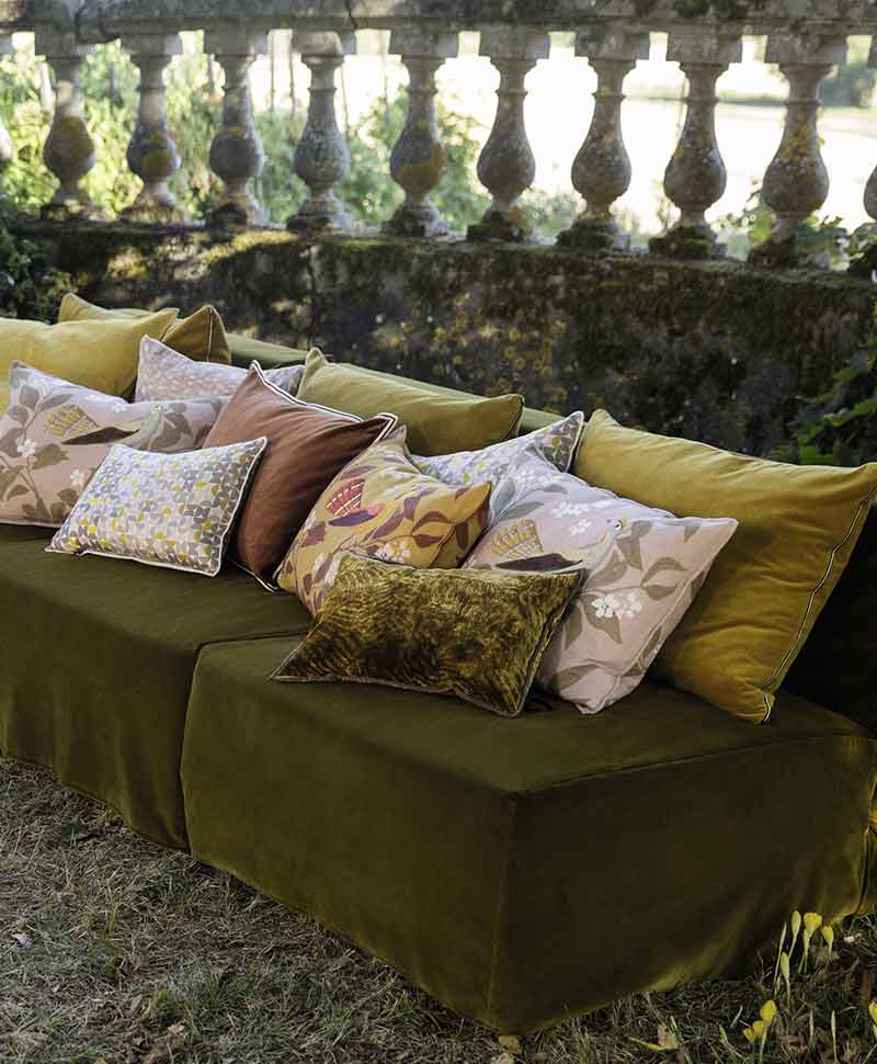 Gemusterte Élitiskissen in Gelb, Grün- und Rosatönen sind auf einem dunkelgrünen Sofa arrangiert, das auf einer Wiese im Freien steht