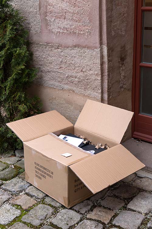 Ein wiederverwendeter Karton steht geöffnet in einem Hof - im Karton befindet sich verpackte Ware vom RAUM concept store