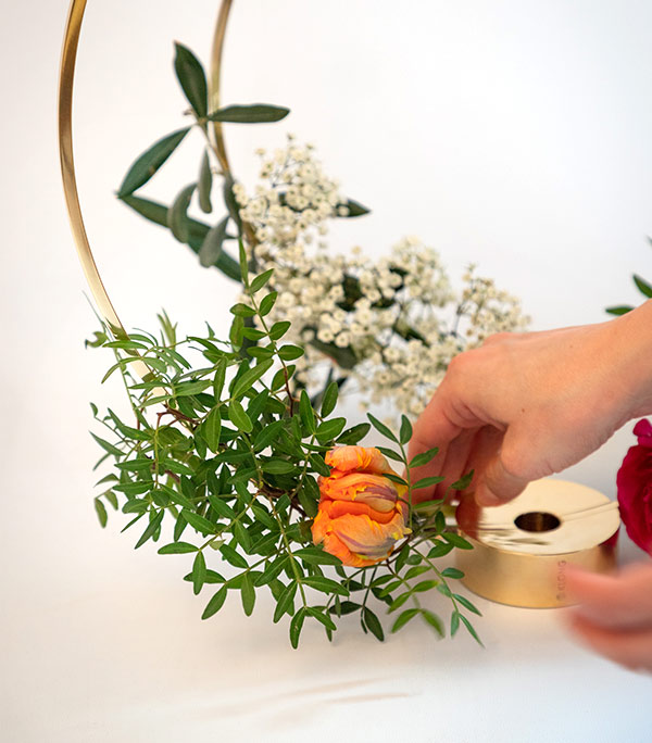 Foto von Händen, wie sie den Kerzenhalter Gloria mit Blumen dekorieren