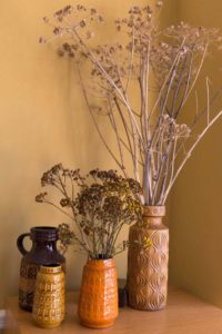 Vier Vasen, die mit Trockenblumen und Zweigen dekoriert wurden, stehen auf einem kleinen Holztisch in einer Ecke