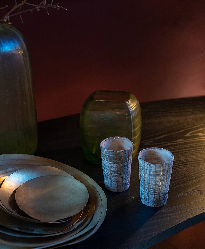 Moodfoto von zwei Keramikbechern von Christine Wagner, die neben einigen ineinandergestellten Schalen und zwei Vasen steht