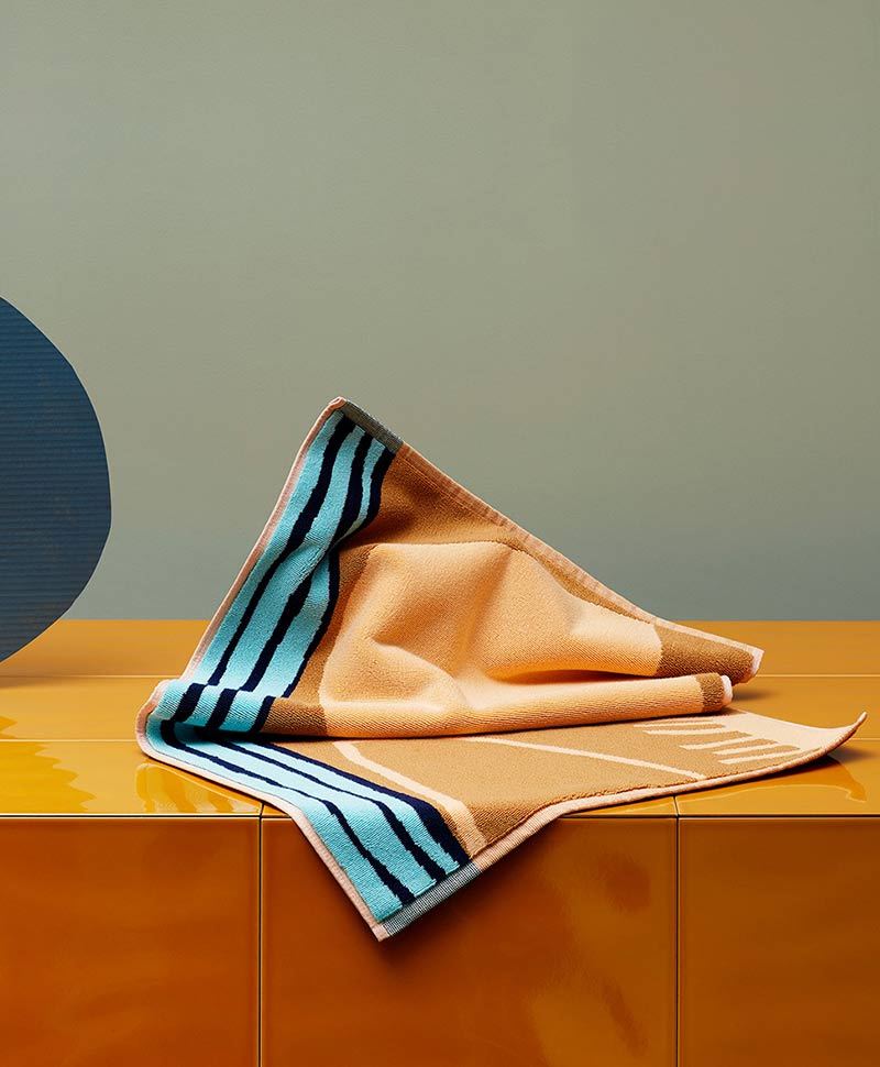 Ein orange-blaues Strandtuch von Frottee di Mare auf einem Tisch