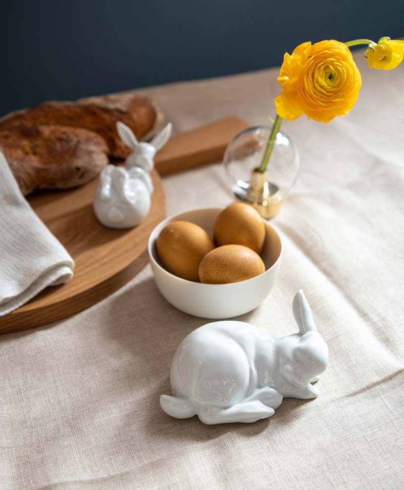 Zwei Porzellanhasen von Fürstenberg auf einem Tisch mit einer Schale mit drei Eiern und einer Blume in einer gläsernen Vase