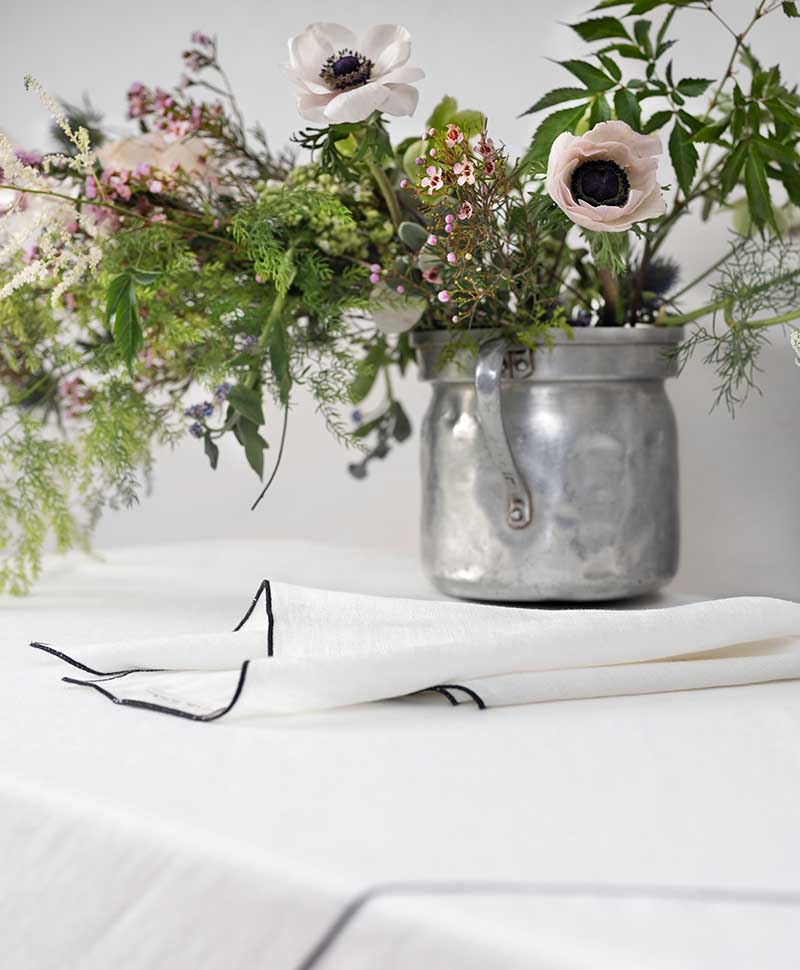 Eine weiße Serviette liegt auf einem Tisch neben einer Pflanze in einem Metalleimer